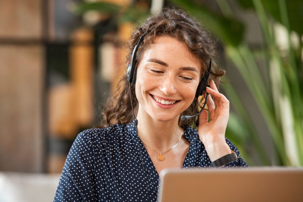 Woman on phone headset working at computer and smiling.